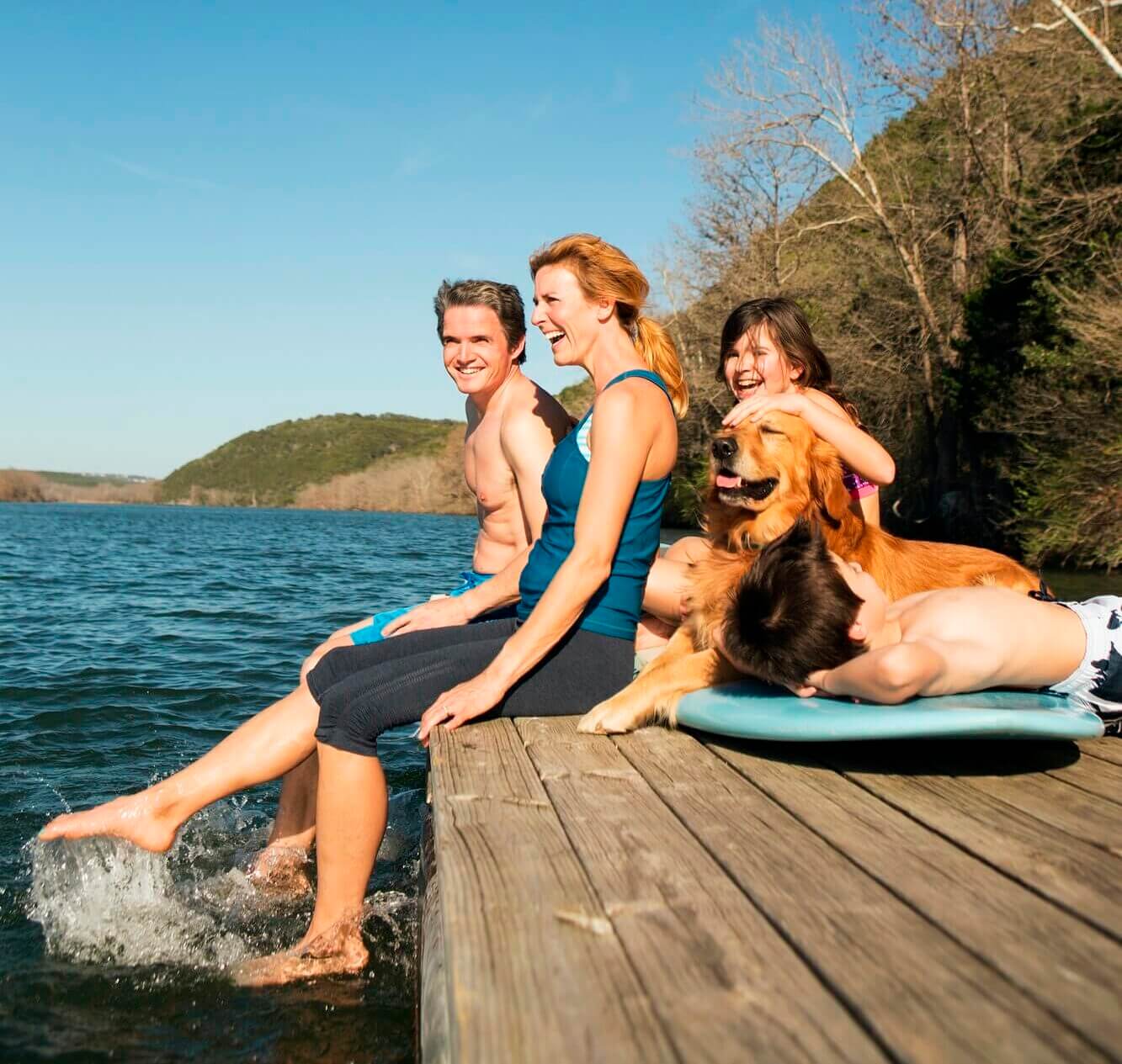 A family and their retriever dog on a jetty by a lake.